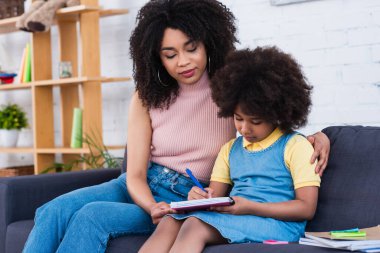 Afrikalı Amerikalı bir kadın, kızına ev ödevlerinde yardım ediyor. 