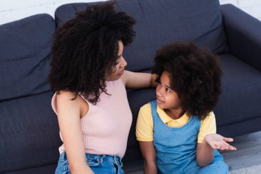 Genç Afro-Amerikan annelerin, kızlarıyla evlerini işaret ederek konuştuklarını yüksek açıdan görüyoruz. 