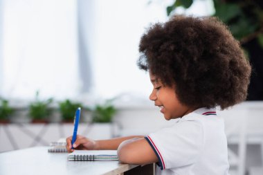 Gülümseyen Afrikalı Amerikalı liseli kızın sınıfta deftere yazdığı yan bakış. 