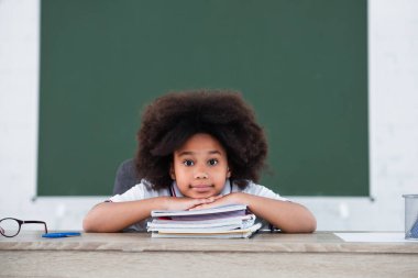 Afrika kökenli Amerikalı okul çocuğu masadaki not defterlerinin yanındaki kameraya bakıyor. 