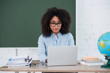 Kitap ve dünyanın yanında çalışırken dizüstü bilgisayar kullanan Afrikalı Amerikalı öğretmen 