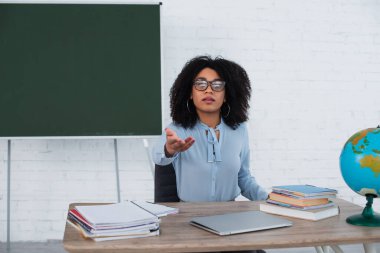 Sınıfta dizüstü bilgisayarın ve not defterlerinin yakınını gösteren Afro-Amerikan öğretmen. 