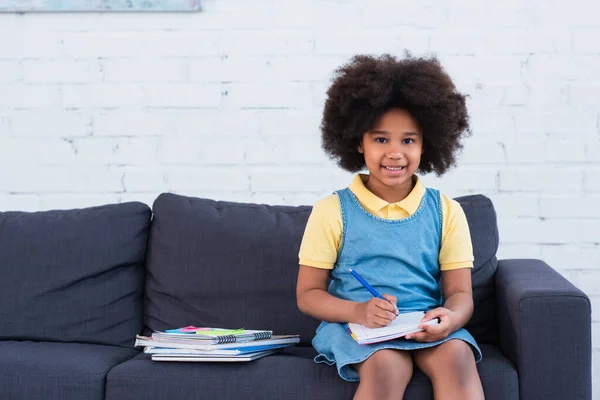 African American Girl Smiling Camera While Doing Schoolwork Couch — Stock Photo, Image