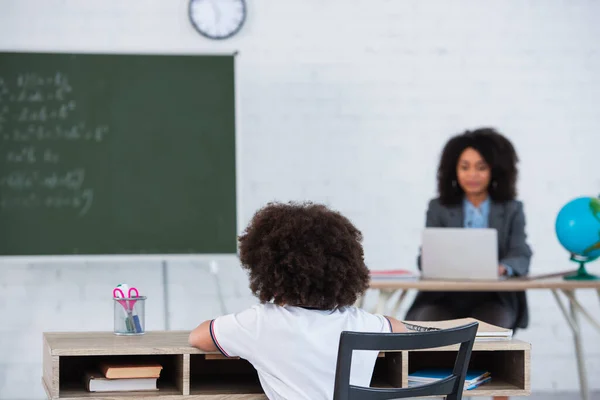 Afroamerikanische Schülerin Sitzt Neben Schreibwaren Und Verschwommenem Lehrer — Stockfoto