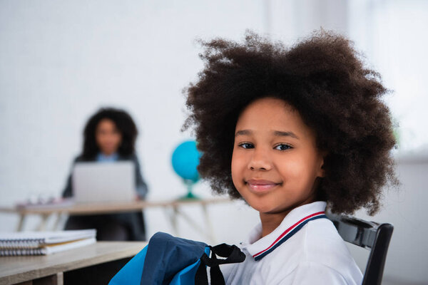 African american schoolkid with backpack looking at camera in classroom 