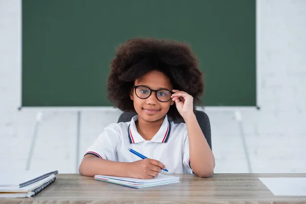 Usmívající Africký Americký Dítě Drží Brýle Pero Blízkosti Notebooky Stole — Stock fotografie