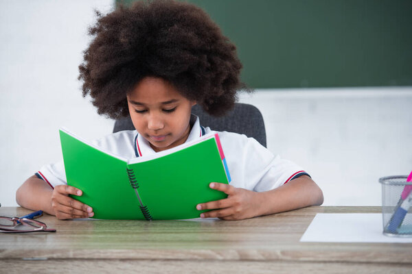 African american schoolgirl looking at notebook in classroom 