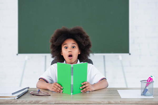 Amazed african american kid holding notebook in classroom 