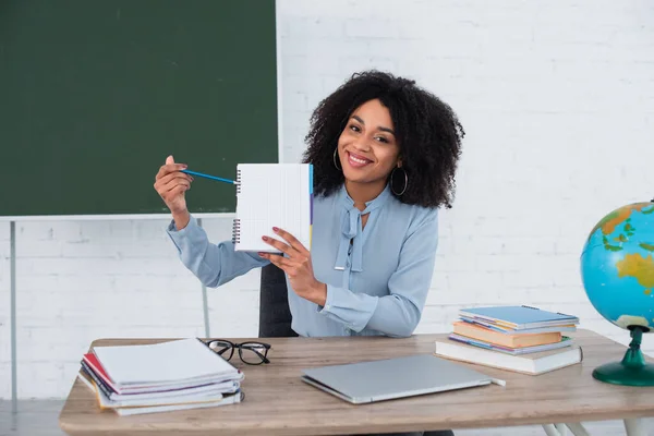 Mosolygó Afro Amerikai Tanár Rámutatva Notebook Közelében Laptop Földgömb Osztályteremben — Stock Fotó