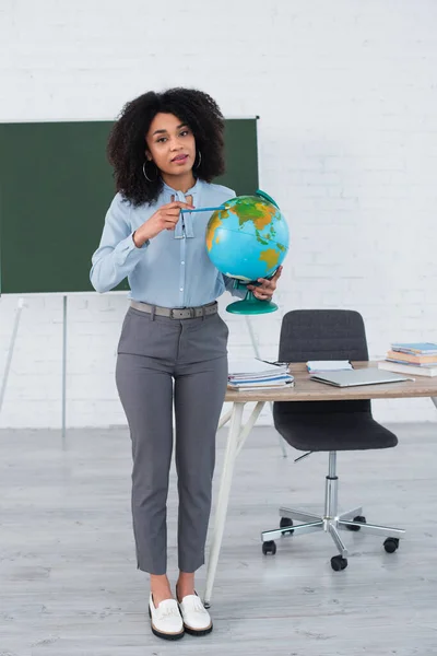 Profesora Afroamericana Apuntando Globo Mirando Cámara Escuela — Foto de Stock