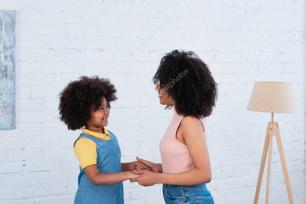 African american mother and daughter holding hands in living room 