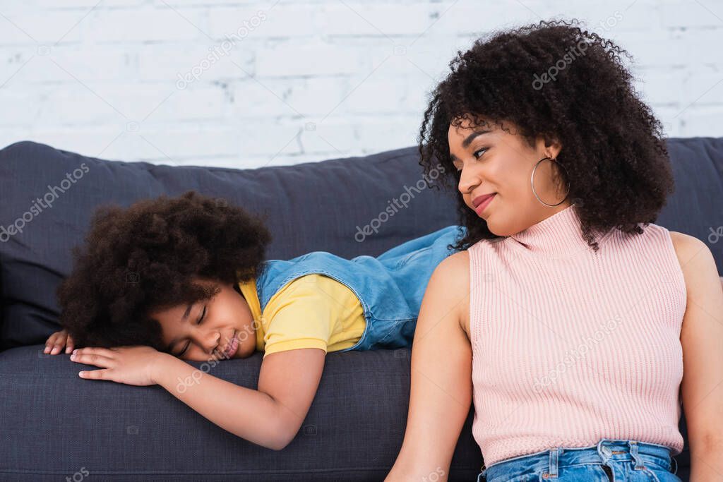 African american mother looking at sleeping daughter on couch in living room 