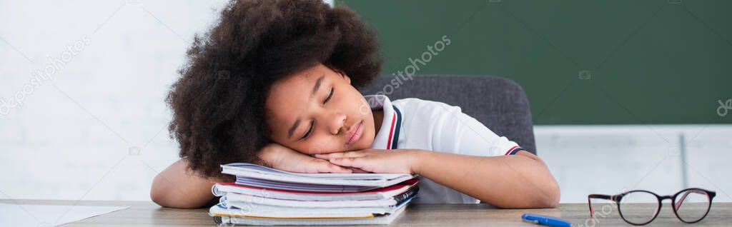 African american child sleeping on copy books in classroom, banner 