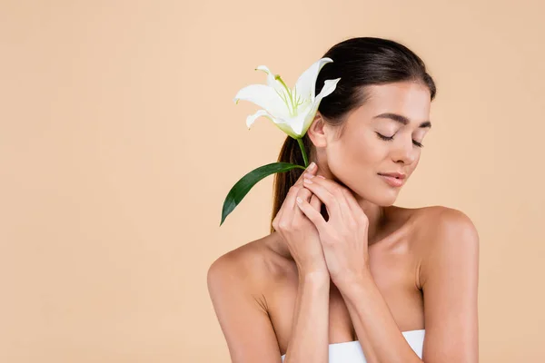 sensual woman with closed eyes posing with white lily isolated on beige, beauty concept