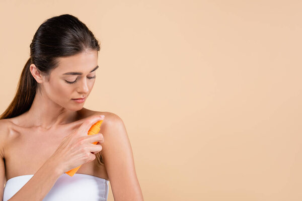 брюнетка женщина распыляя солнцезащитный крем на плечо изолированы на бежевый