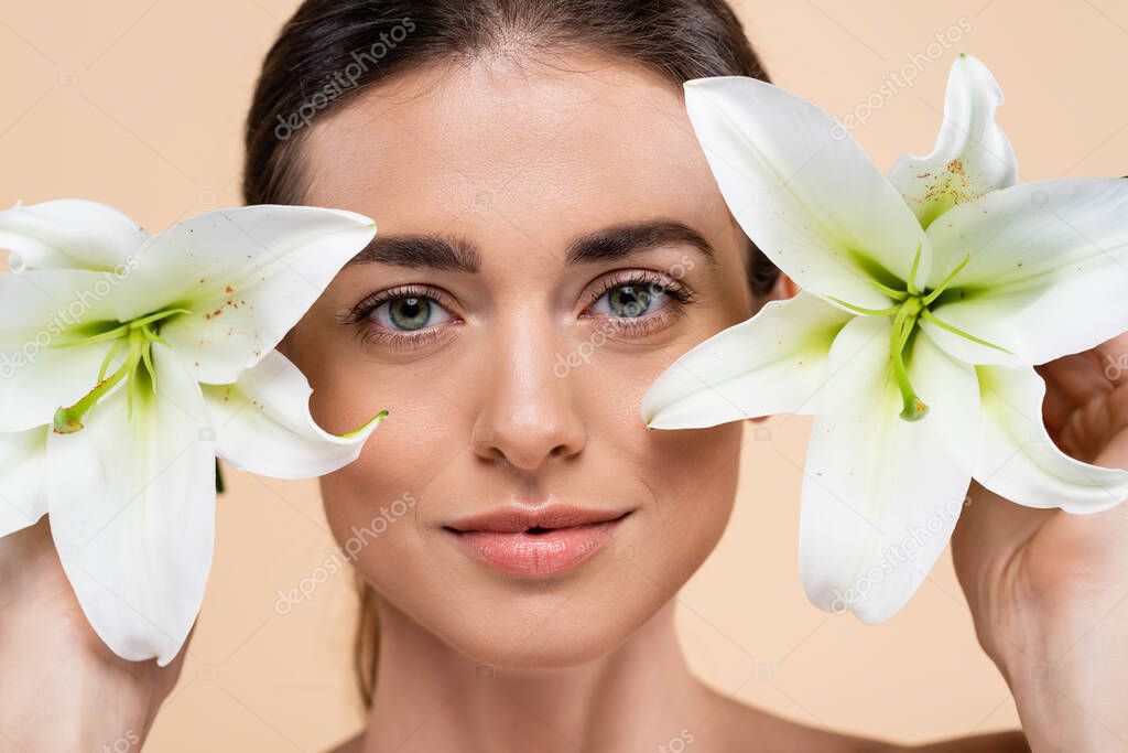 portrait of brunette woman with white lily flowers isolated on beige, beauty concept