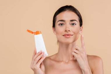 brunette woman holding sunscreen and pointing up with finger isolated on beige clipart