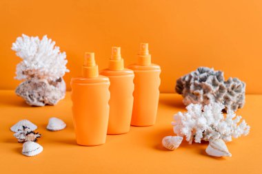 sea corals and bottles with sunscreen on orange background clipart