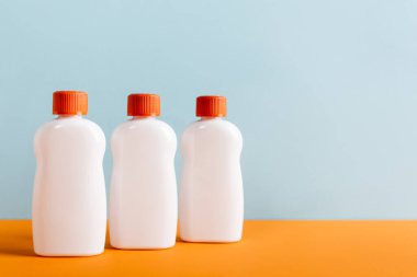 Turuncu yüzeyde beyaz güneş kremi şişeleri mavi renkte izole edilmiş.