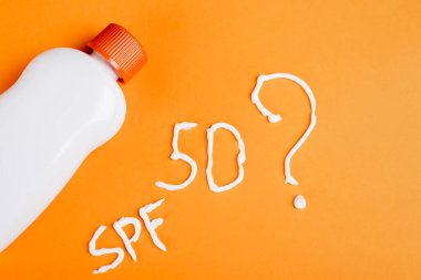 Spf harflerinin yanındaki güneş kreminin üst görünümü, 50 numara ve turuncu arkaplanda soru işareti