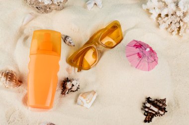 top view of orange sunglasses and sunscreen on sand near seashells clipart