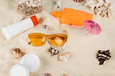 top view of containers with sunscreen and cosmetic cream near sunglasses and seashells on sand clipart