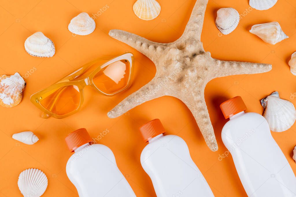 top view of starfish, seashells, sunglasses and white bottles of sunscreen on orange