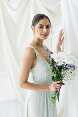 Neşeli bir kadın elinde çiçeklerle beyaz elbiseler içinde.