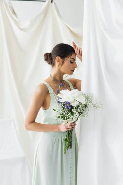 Güzel ve esmer bir kadın beyaz çiçekle poz veriyor.