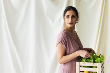 Güzel bir kadın elinde beyaz sebzeli tahta kutu tutuyor.