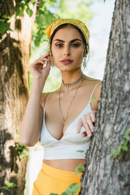 Sarı başörtülü moda kadın ağaç gövdesinin yanında poz veriyor.