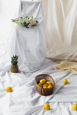 Ananas sepetinde olgun limonlar beyaz çarşafların üzerinde, çiçek buketinin yanında. 