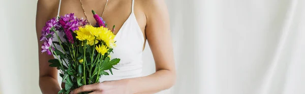 cropped view of woman in crop top holding flowers on white, banner