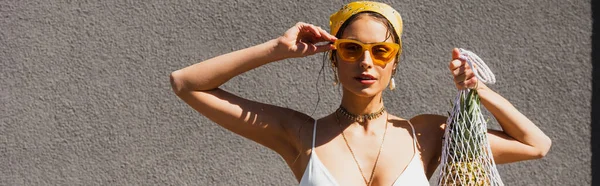 Stylish Woman Adjusting Sunglasses Holding String Bag Pineapple Concrete Wall — Stock Photo, Image