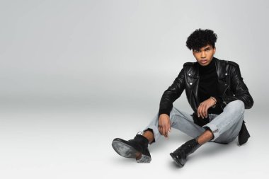 african american man in trendy clothes looking at camera while sitting on grey 