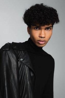 african american man in black turtleneck and leather jacket on shoulder looking at camera isolated on grey