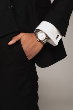 cropped view of african american man in black formal wear and wristwatch holding hand in pocket isolated on grey clipart