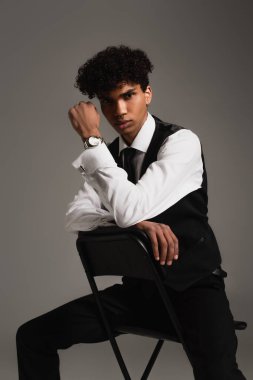 young african american man in white shirt and black vest sitting isolated on grey