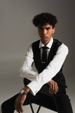 african american businessman in elegant clothes looking at camera while sitting on grey 
