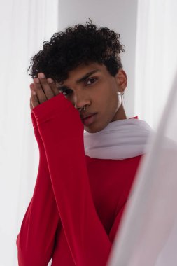 young african american man with praying hands looking at camera near white transparent cloth