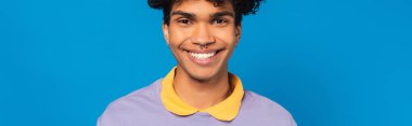 pleased african american man with piercing looking at camera isolated on blue, banner