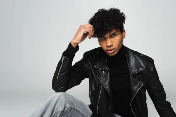 young african american man in leather jacket and jeans looking at camera isolated on grey