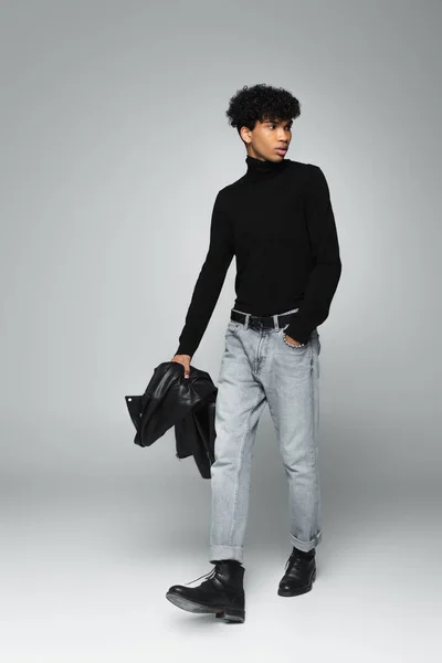 trendy african american man walking with hand in pocket of jeans on grey background