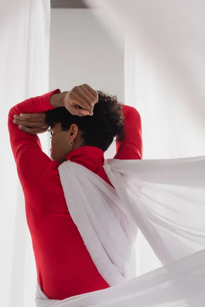 back view of african american man in red turtleneck posing in white chiffon drapery