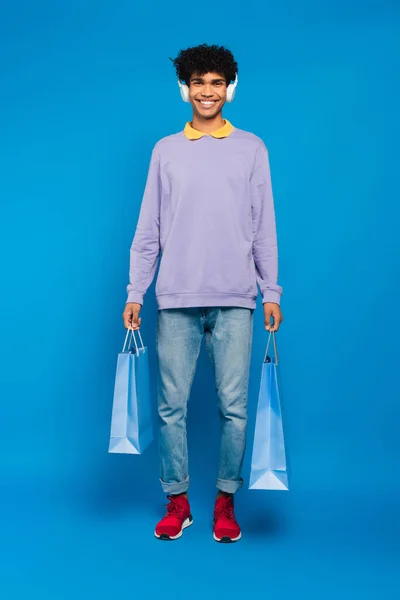 Довольный Африканский Американец Наушниках Стоящий Сумками Покупок Синем Фоне — стоковое фото