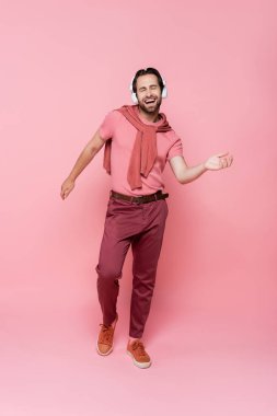 Gözleri kapalı bir adam pembe arka planda kulaklıkla müzik dinlerken şarkı söylüyor.