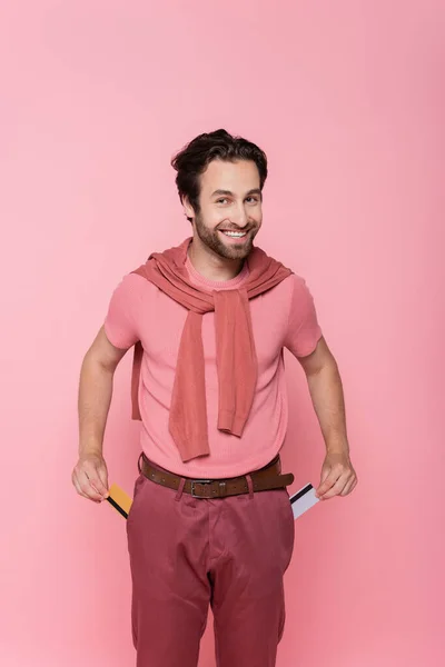 Hombre Sonriente Sosteniendo Tarjetas Crédito Cerca Bolsillos Pantalones Aislados Rosa — Foto de Stock