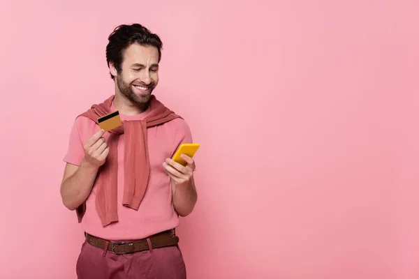 Positive Man Holding Credit Card Using Cellphone Isolated Pink — Stock Photo, Image