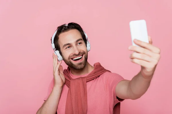 Kulaklıklı Gülümseyen Adam Pembe Renkteki Bulanık Akıllı Telefondan Selfie Çekiyor — Stok fotoğraf