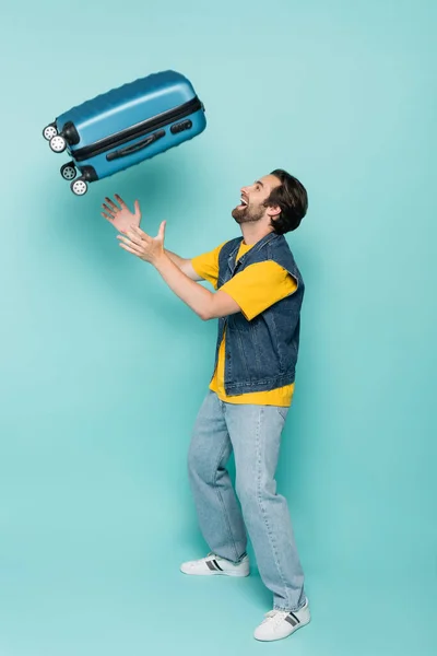 一个快乐的男人把手提箱扔在蓝色的背景下的侧视图 — 图库照片